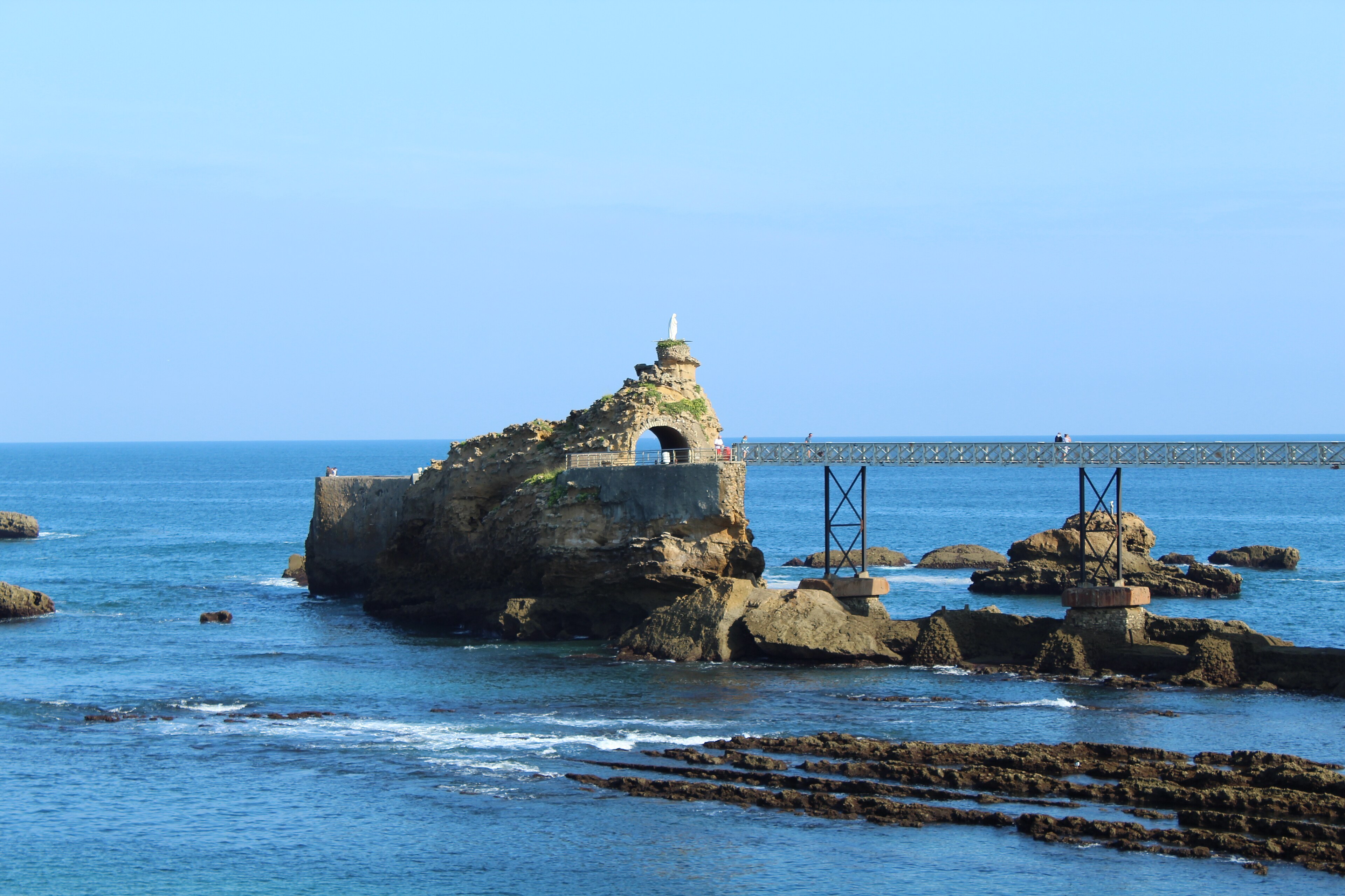 Rocher de la Vierge à Biarritz, passerelle métallique, statue, arché et mer calme.