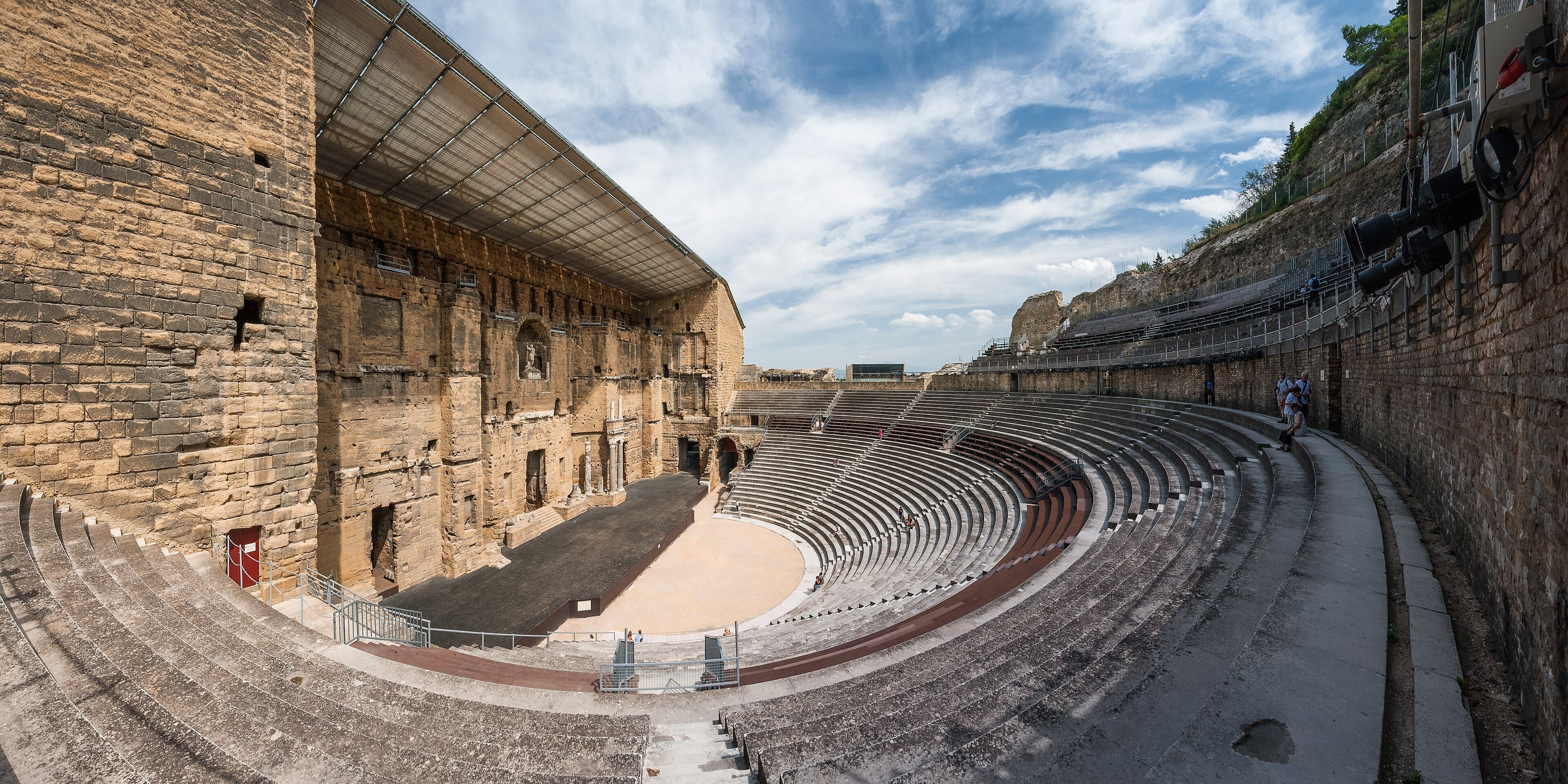 Cavea du théâtre antique d’Orange, mur de scène, auvent moderne et gradins sous un ciel d’été.