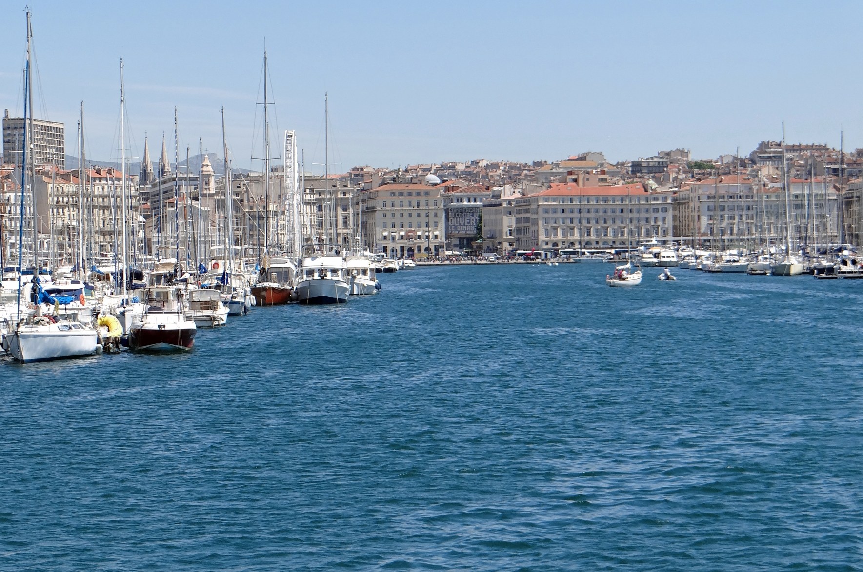 Vieux-Port de Marseille : voiliers à quai, façades du quai, colline et clocher au fond, ciel clair.